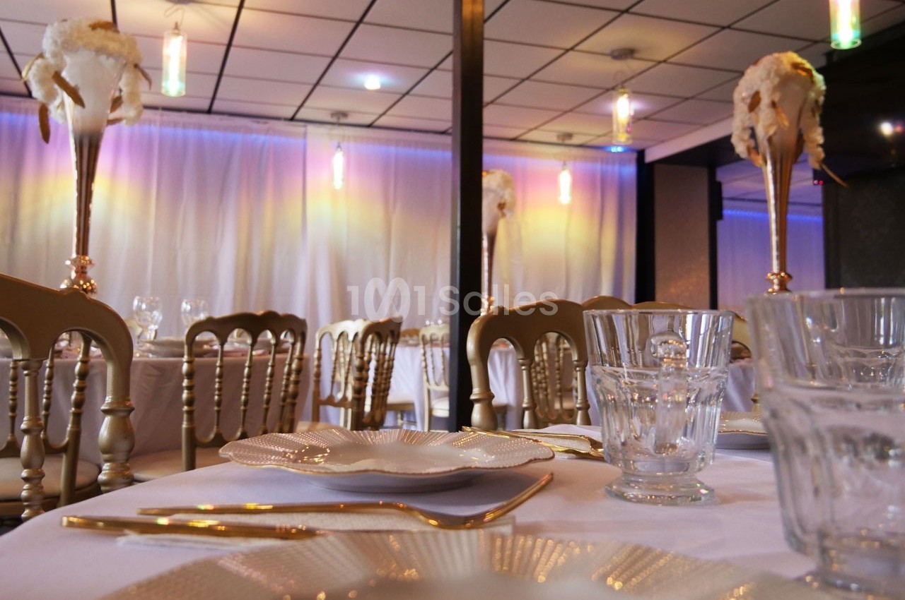 Salle de réception élégante avec tables dressées, chaises dorées et centres de table ornés de fleurs blanches.