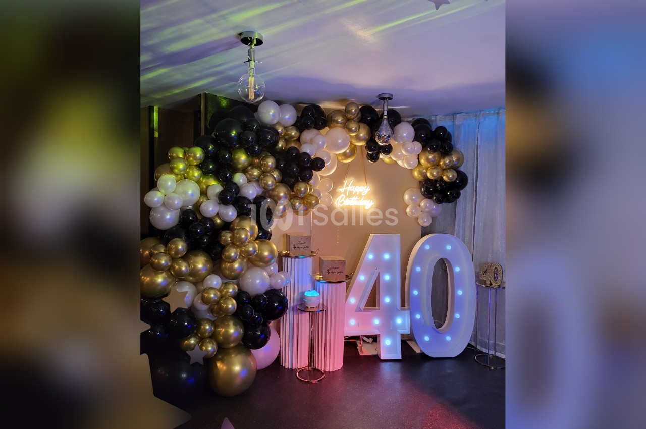 Décoration d'anniversaire avec ballons noirs, blancs et dorés, chiffres lumineux ’40’ et enseigne ’Happy Birthday’.