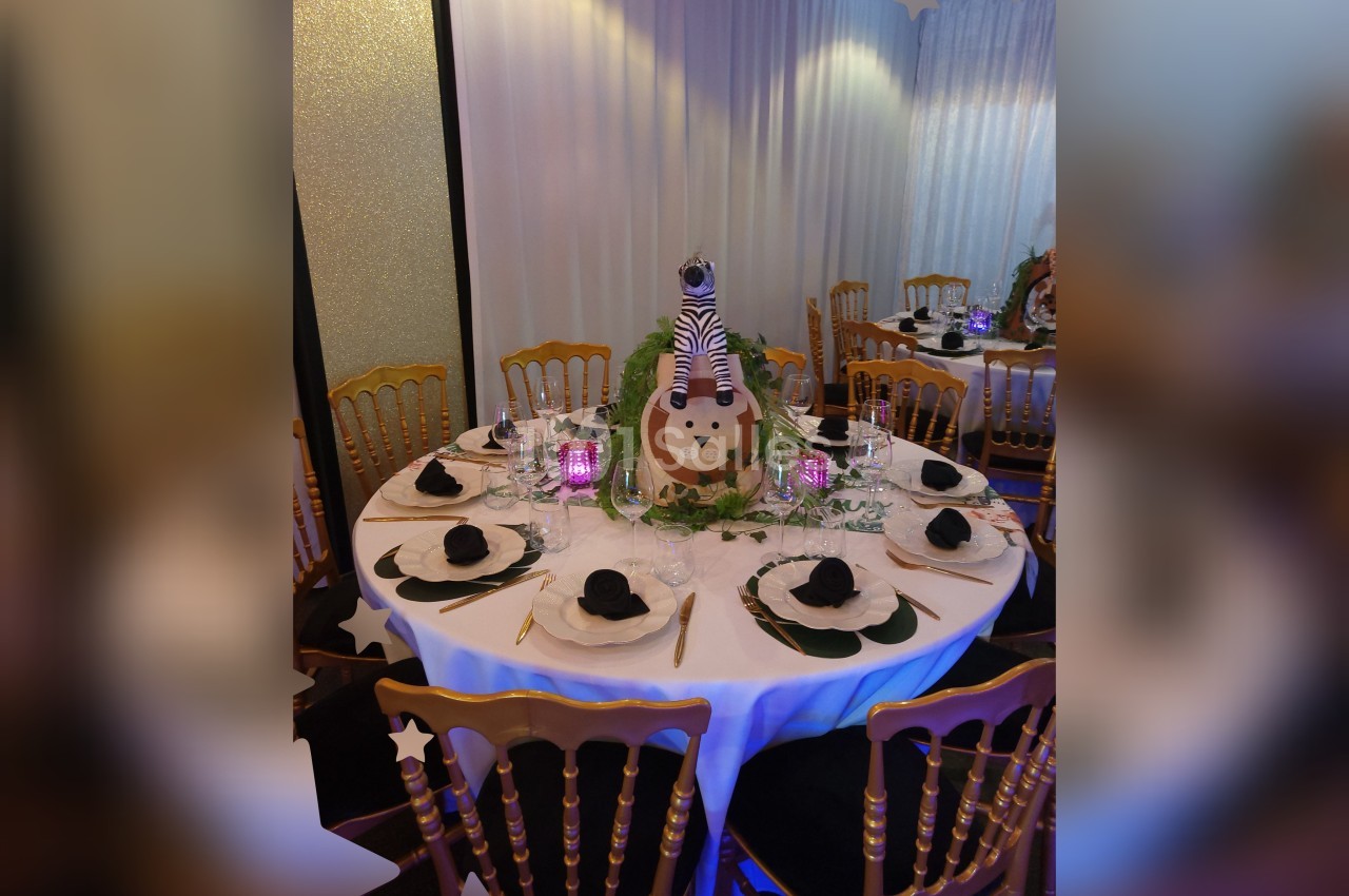 Table ronde décorée sur le thème safari avec centre de table lion, serviettes noires pliées et chaises dorées.