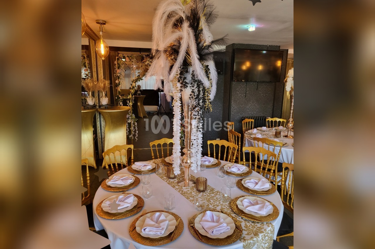 Table ronde élégamment dressée avec nappes dorées, serviettes pliées, assiettes décoratives et centre de table floral.