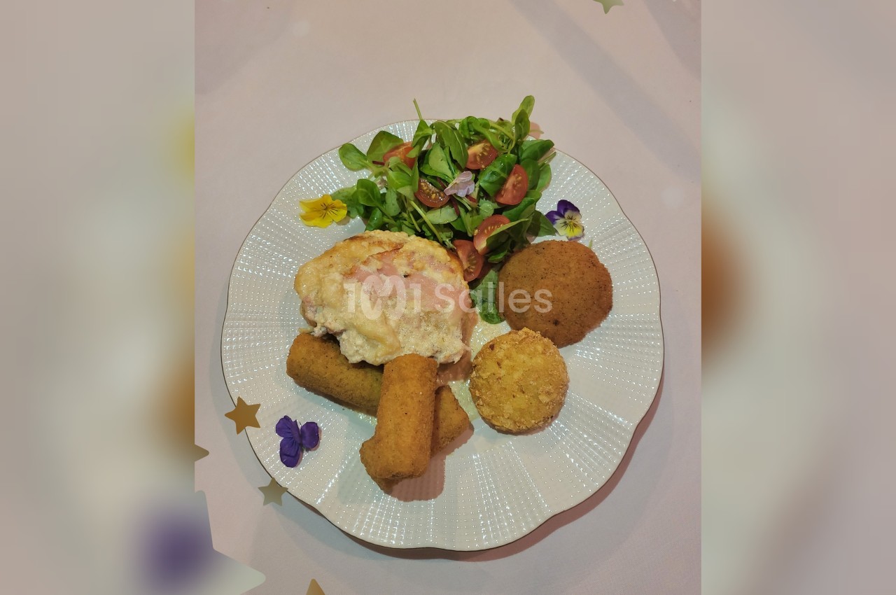 Assiette composée de croquettes, d'une escalope gratinée, d'une salade verte avec tomates et fleurs comestibles.