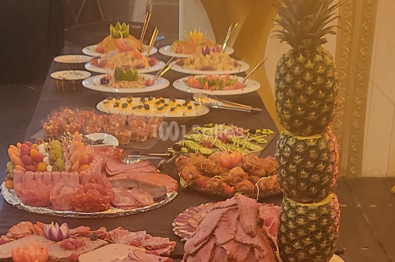 Buffet avec plats variés, incluant charcuterie, fruits, desserts et une décoration d'ananas empilés.