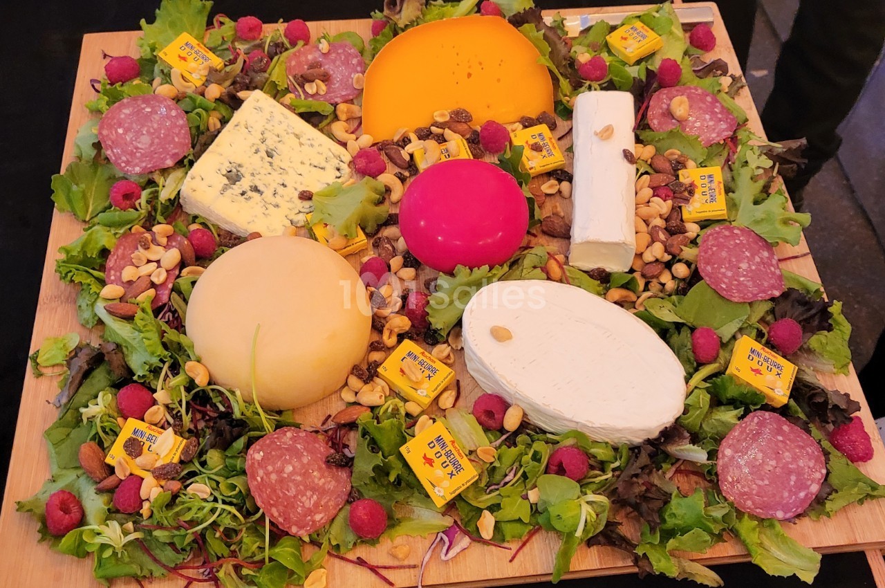 Plateau garni de fromages variés, charcuterie, framboises, noix et salade sur une planche en bois.