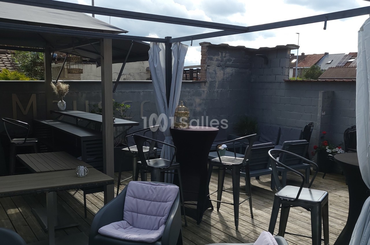 Terrasse en bois aménagée avec des tables, chaises et parasols, entourée de murs gris et partiellement couverte.