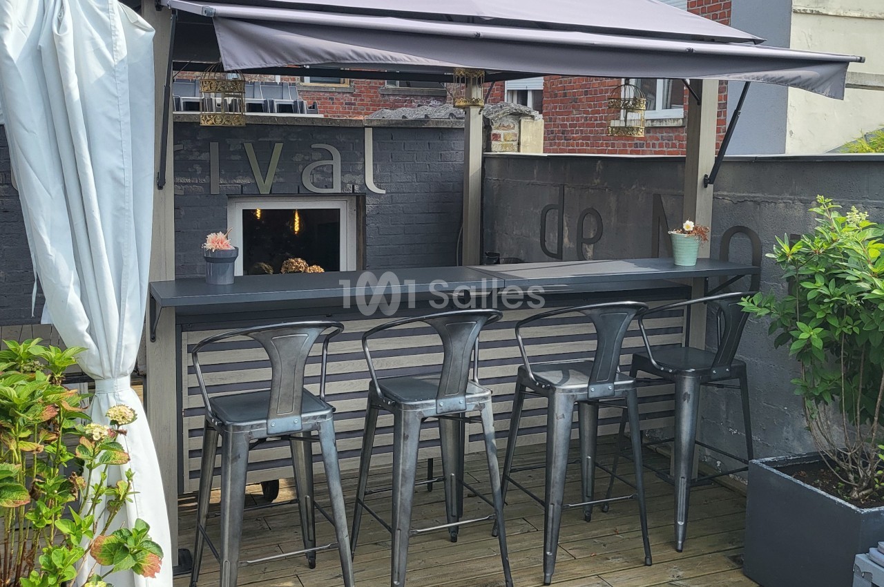 Bar extérieur avec tabourets en métal, comptoir en bois, pergola et plantes sur une terrasse en bois.