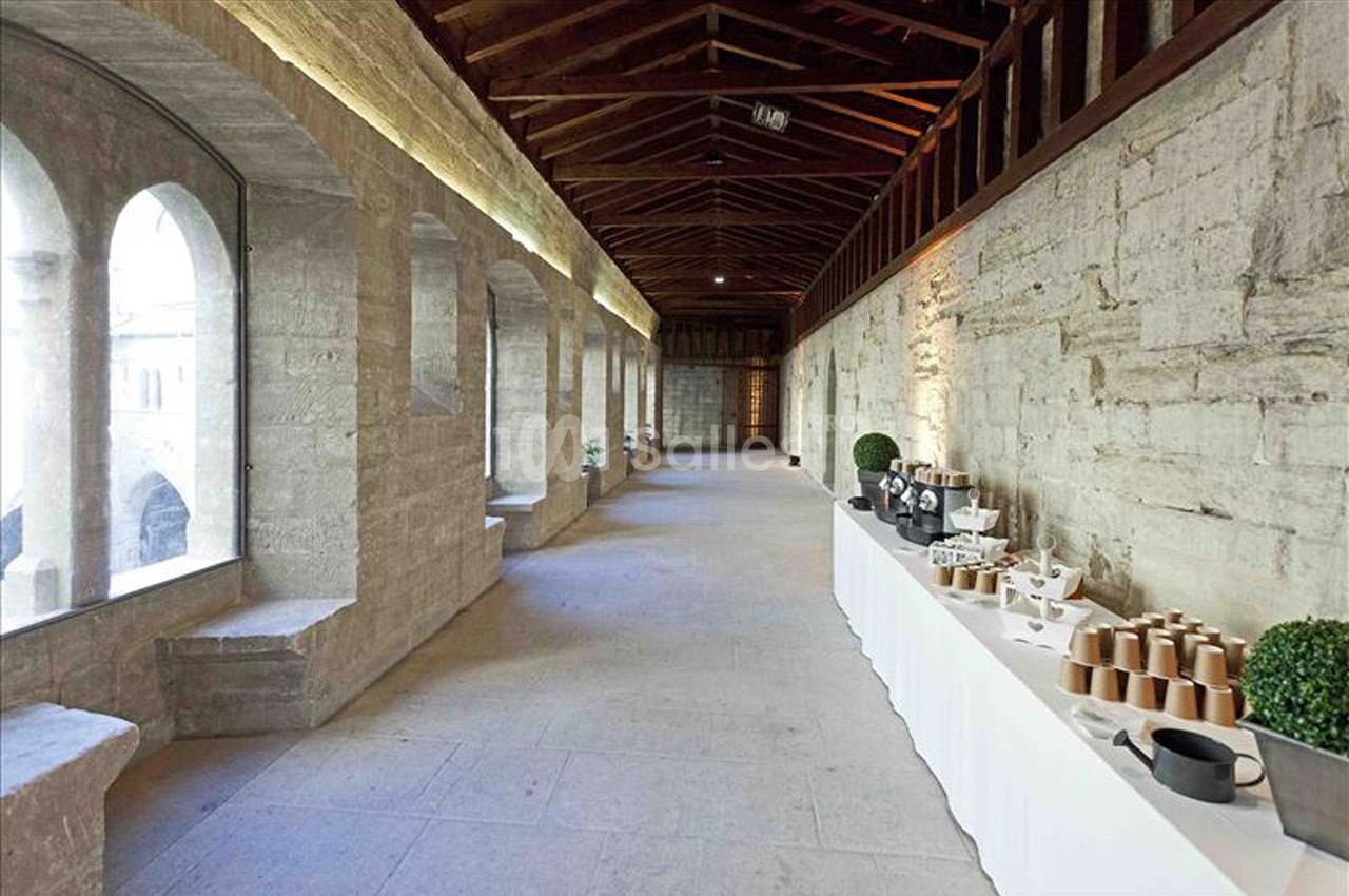 Un couloir en pierre avec des arches vitrées à gauche et une table de service dressée à droite.