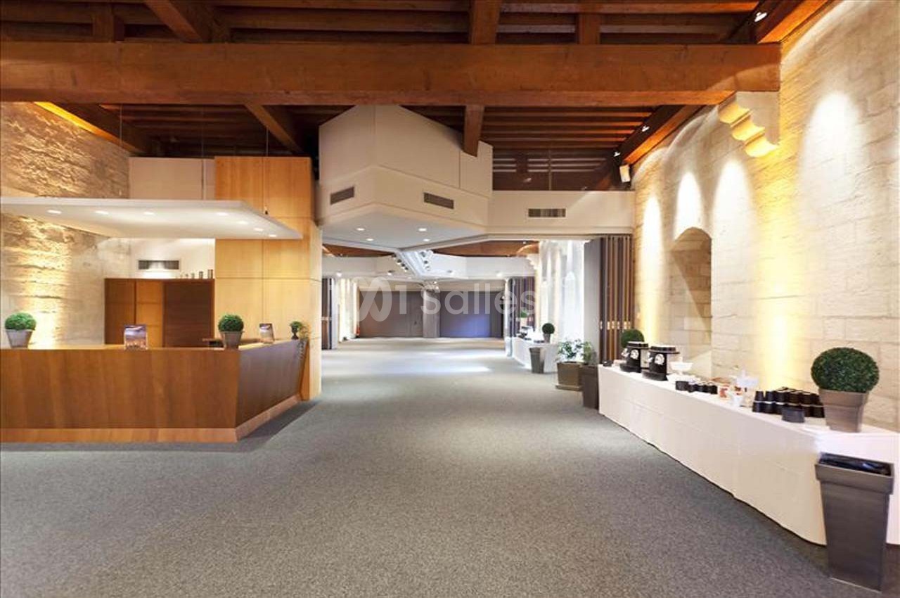 Salle spacieuse avec plafond en bois, murs en pierre, comptoir en bois et tables dressées sur la droite.