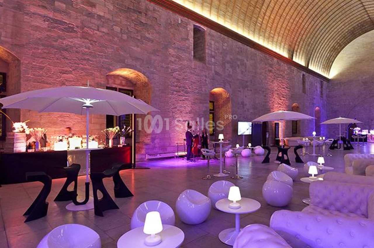 Salle voûtée éclairée de lumières colorées, aménagée avec des fauteuils modernes, des parasols et un bar.