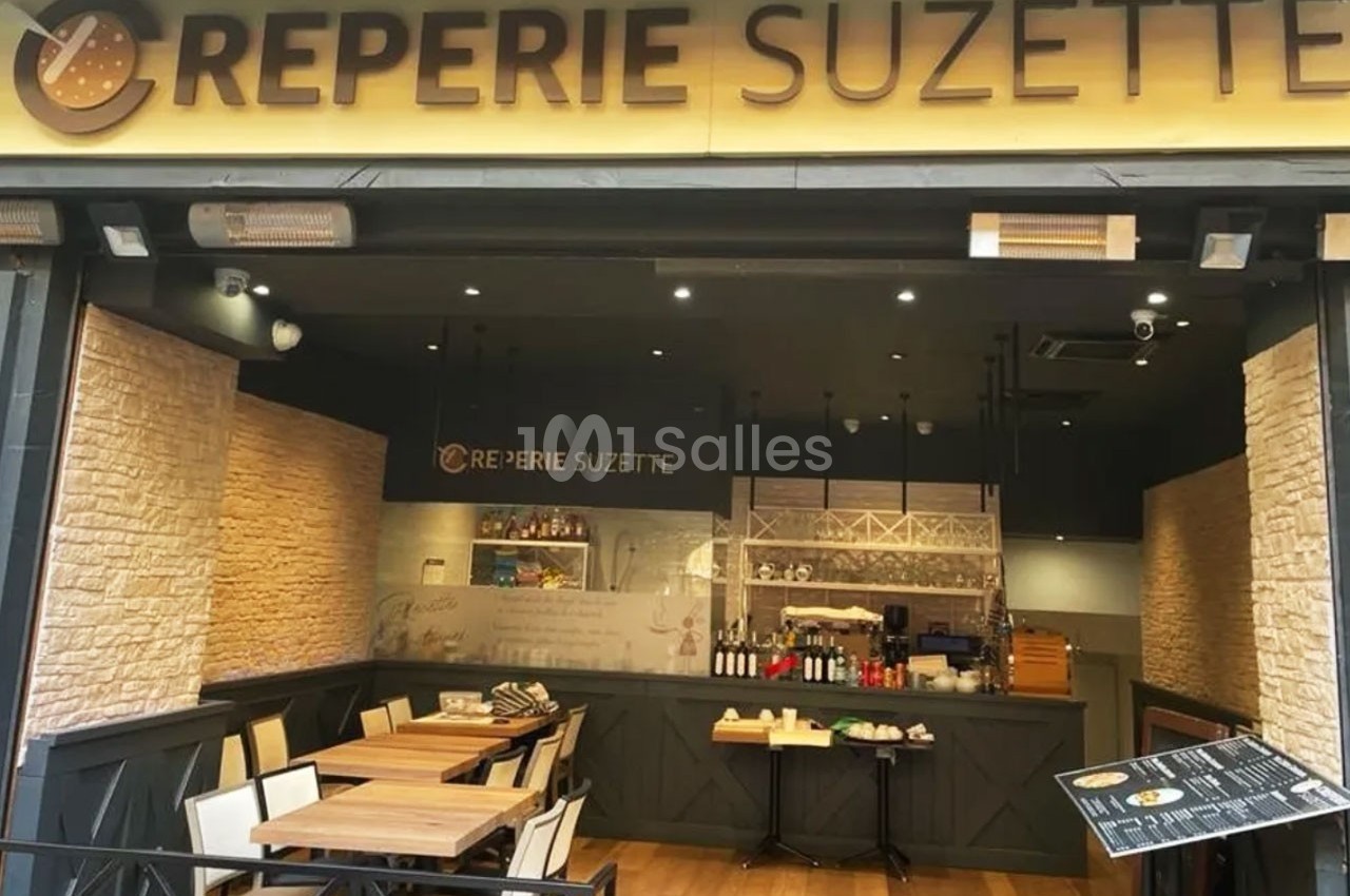 Façade d'une crêperie avec terrasse en bois, tables et chaises, et un comptoir visible à l'intérieur.