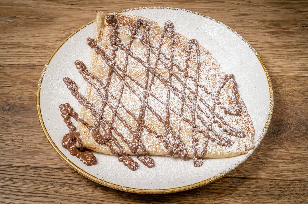Crêpe pliée garnie de chocolat fondu et saupoudrée de sucre glace, servie sur une assiette blanche.