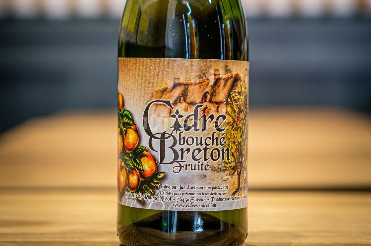 Bouteille de cidre bouché breton fruité avec une étiquette illustrée de pommes et de motifs rustiques.