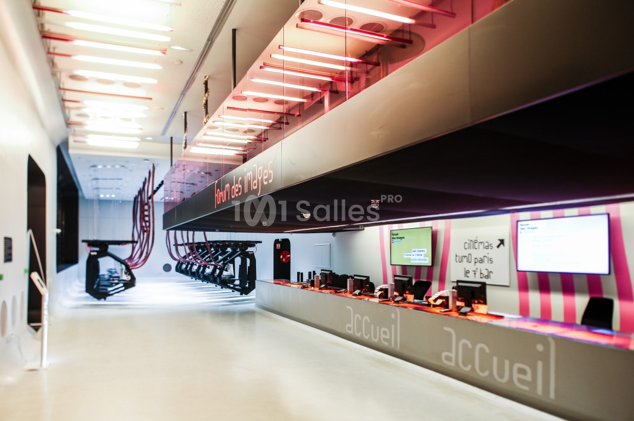 Comptoir d'accueil moderne avec signalétique lumineuse, écrans d'information et espace de fitness en arrière-plan.