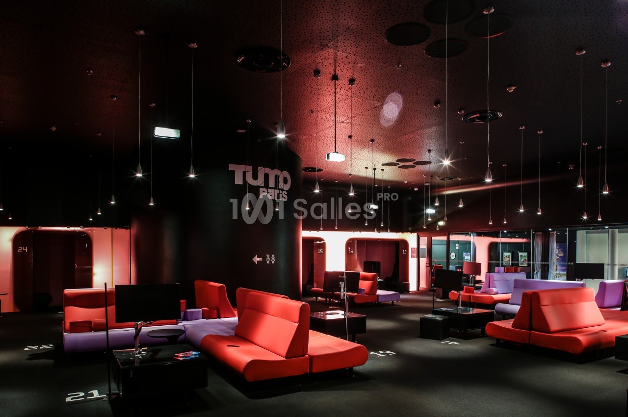 Espace intérieur moderne avec canapés colorés, éclairage suspendu et logo ’TUMO Paris’ sur un mur noir.