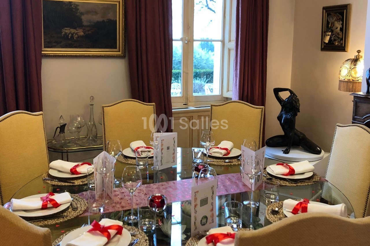 Salle à manger élégante avec table ronde dressée, nappes blanches, rubans rouges et décoration raffinée.