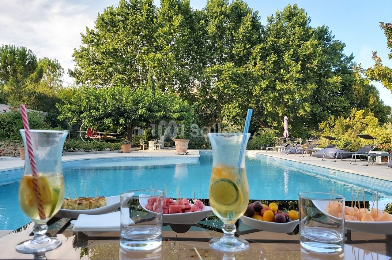 Verres de boissons fraîches et assiettes de collations disposés sur une table près d'une piscine entourée de verdure.