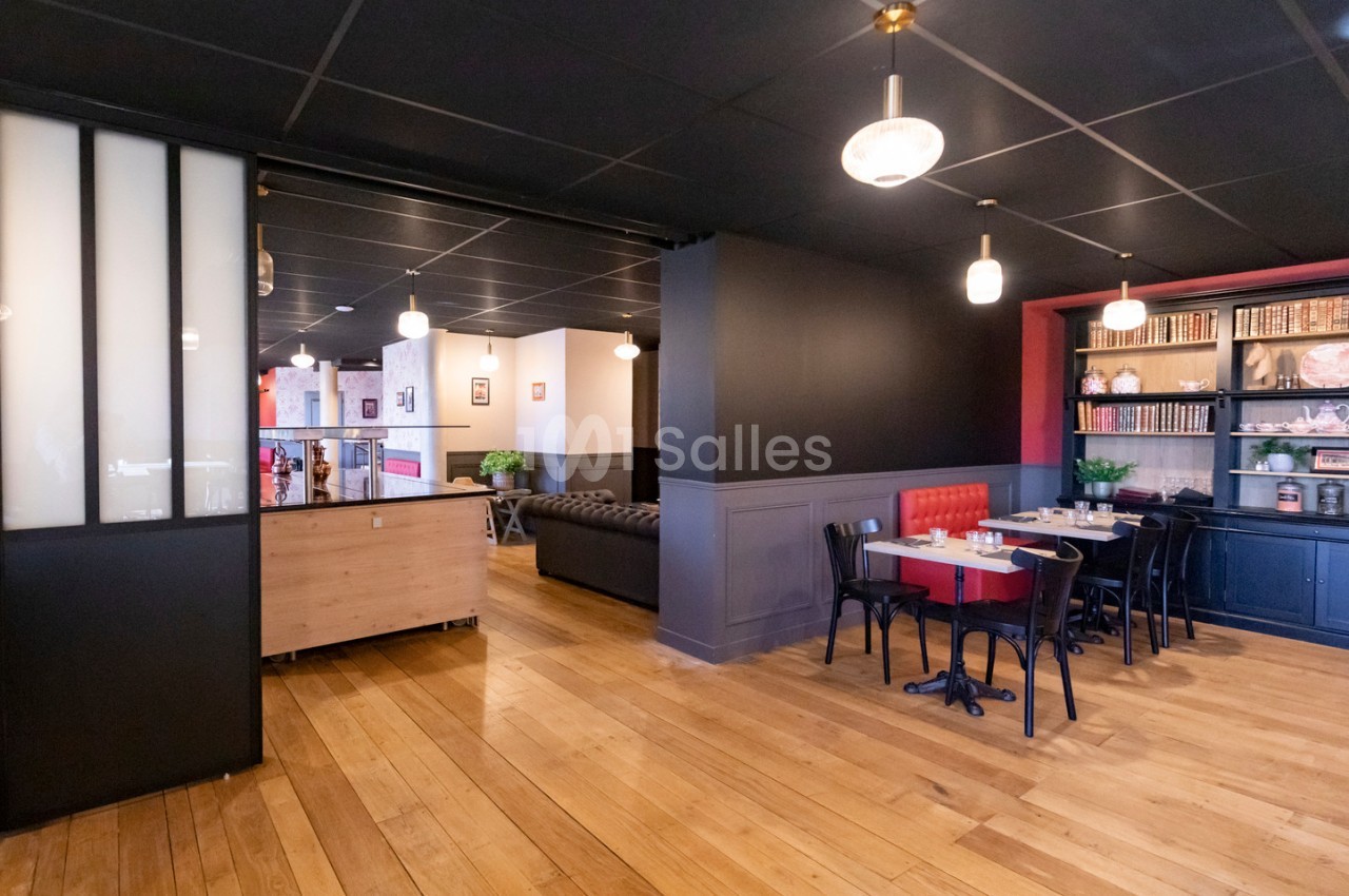 Salle de restaurant lumineuse avec parquet en bois, tables dressées, étagères décoratives et banquette rouge.