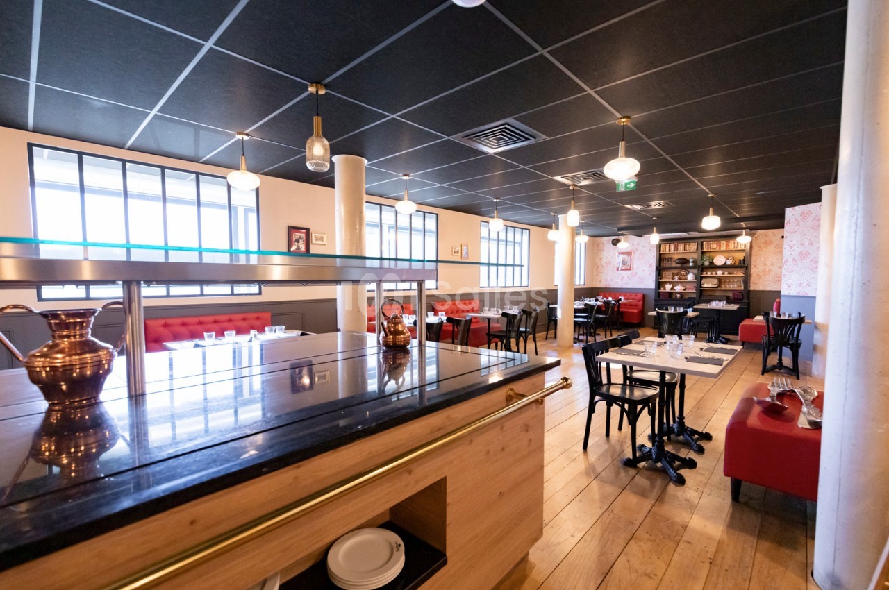 Salle de restaurant lumineuse avec tables dressées, banquettes rouges et décoration moderne.