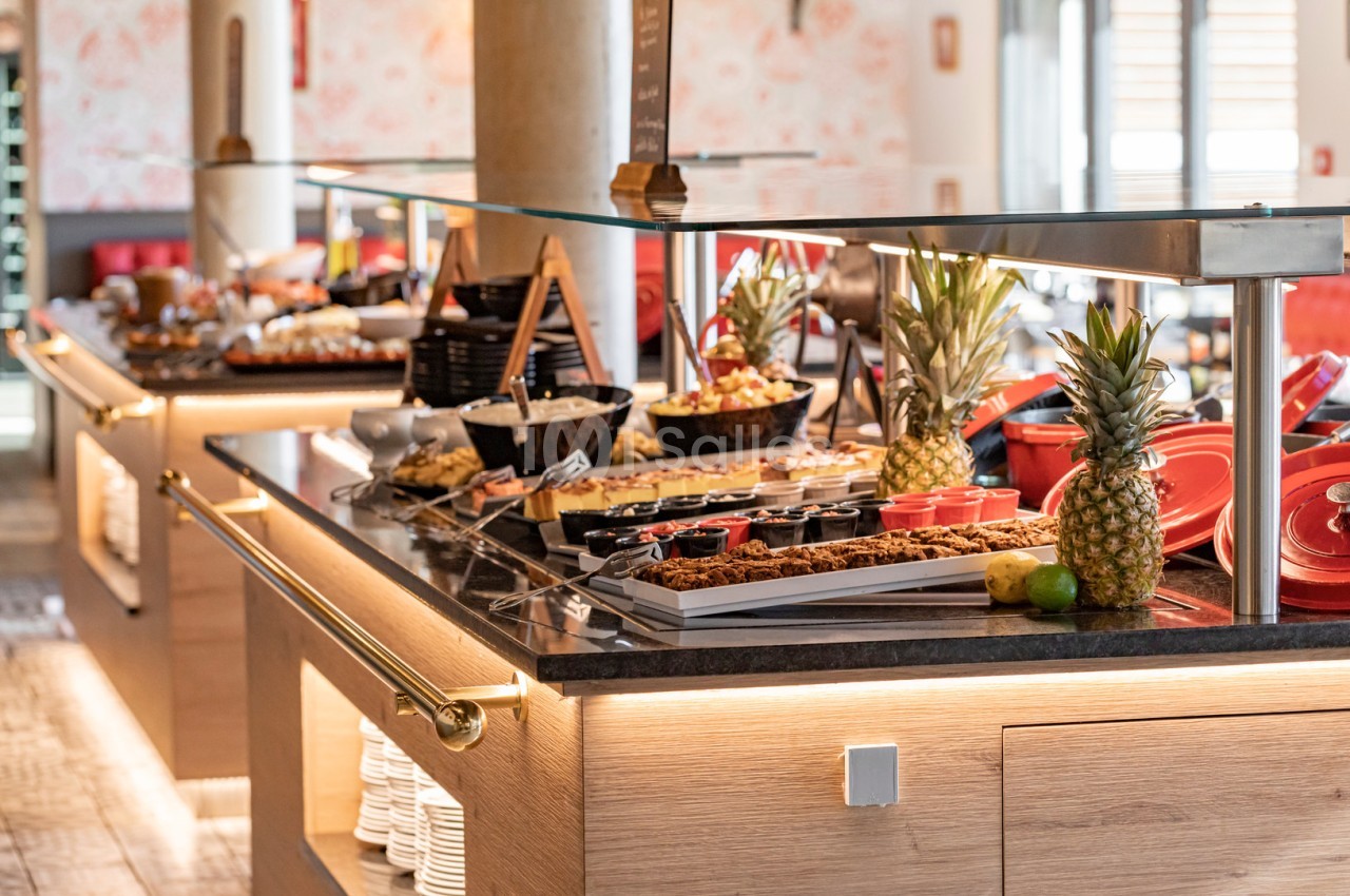 Buffet varié avec fruits, plats chauds et froids, présenté sur un comptoir en bois dans un espace lumineux.