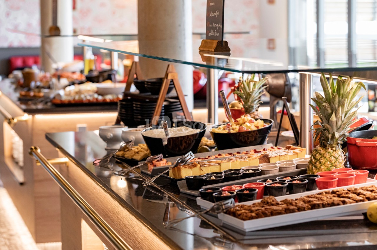 Buffet varié avec desserts, fruits frais, plats salés et boissons disposés sur un comptoir en verre.