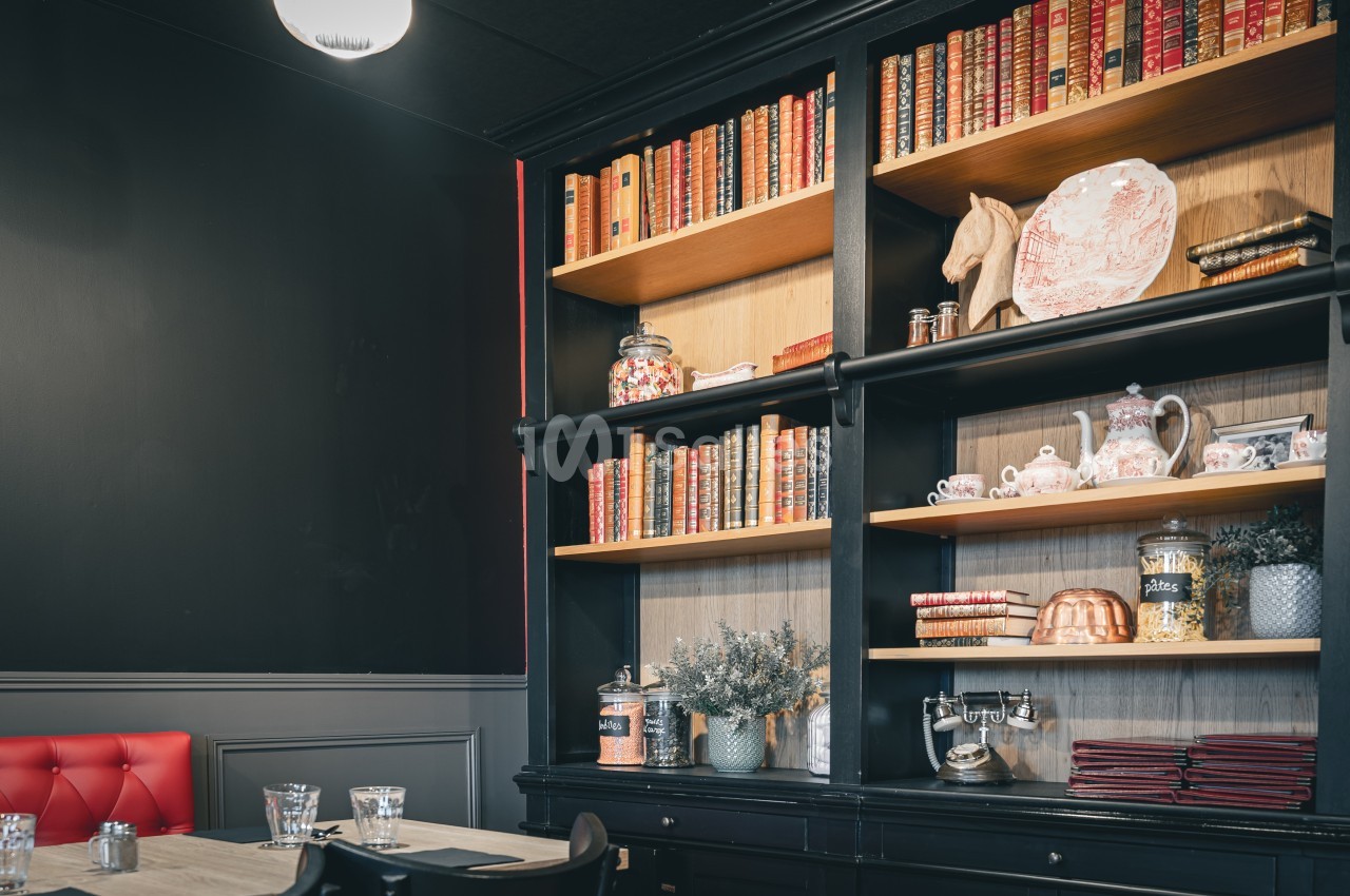 Bibliothèque en bois noir avec livres anciens, objets décoratifs et vaisselle, dans une pièce au style vintage.