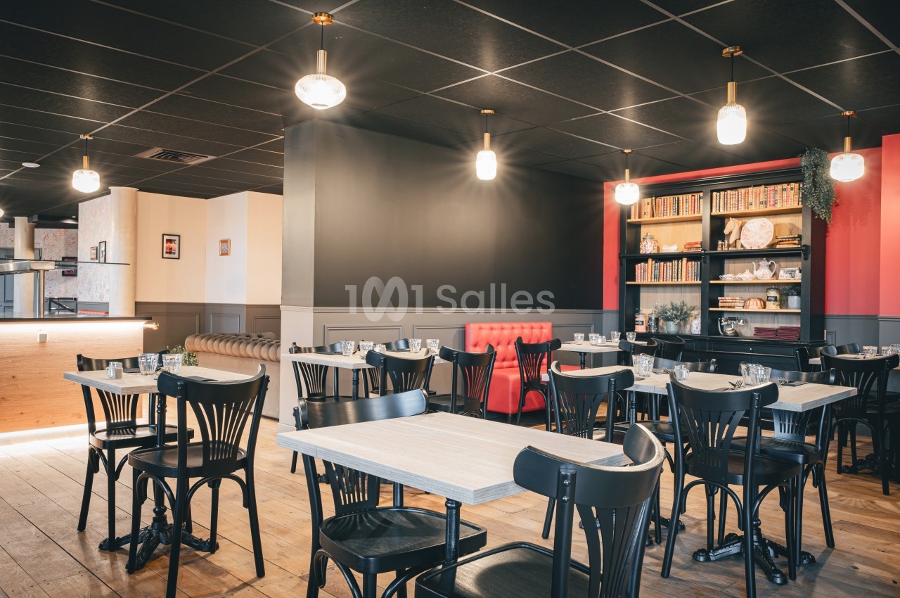 Salle de restaurant lumineuse avec tables en bois, chaises noires, étagère décorative et banquette rouge.
