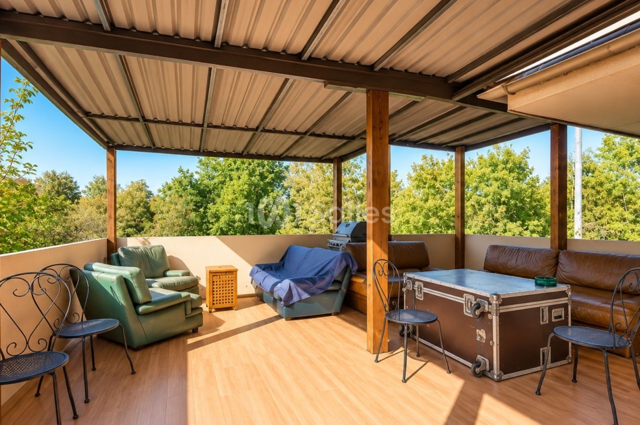 Terrasse couverte avec mobilier varié, incluant fauteuils, canapé, table et vue sur des arbres en arrière-plan.