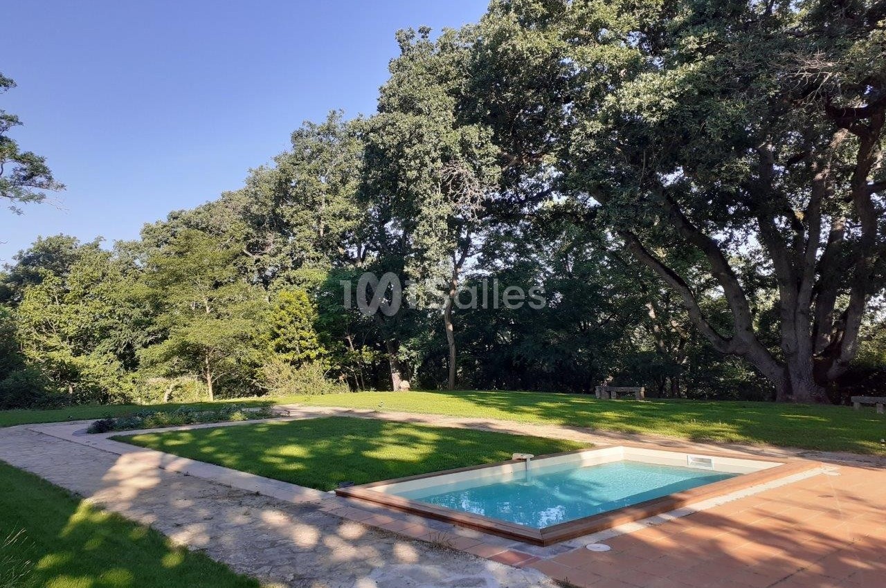 Piscine rectangulaire entourée de pelouse et d'arbres, avec un chemin en pierre à proximité, sous un ciel dégagé.