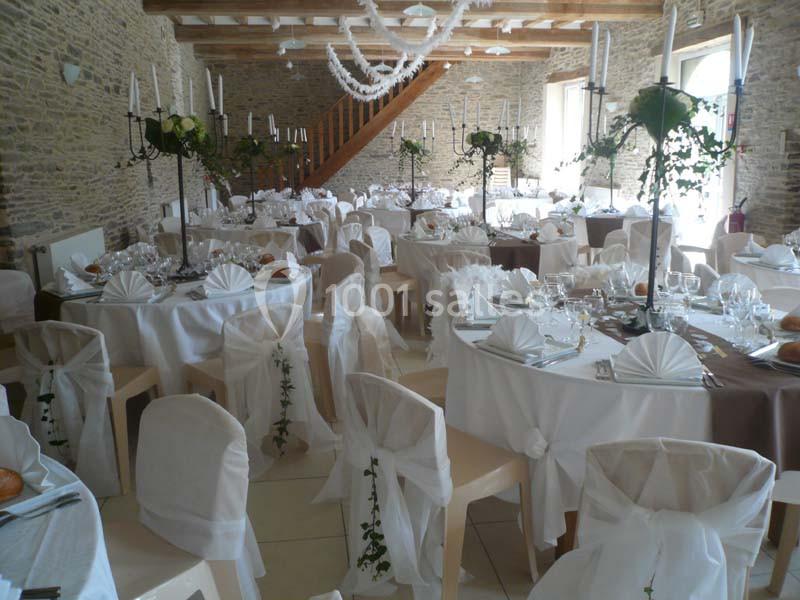 Salle de réception décorée avec des tables rondes, nappes blanches, serviettes pliées et chandeliers ornés de feuillage.