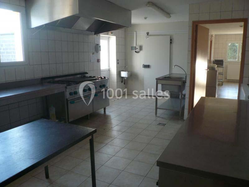 Cuisine professionnelle avec équipements en inox, plan de travail, four, hotte et carrelage au sol et aux murs.