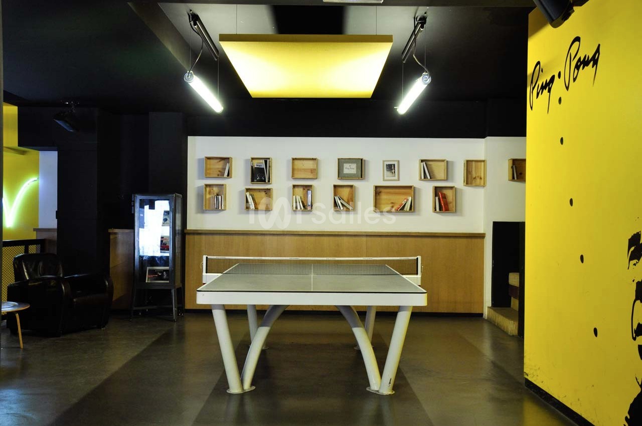 Table de ping-pong dans une pièce moderne avec étagères murales, fauteuil et décorations jaunes et noires.