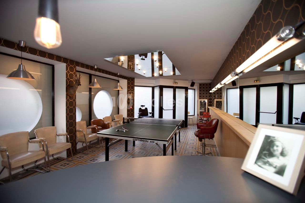 Salle lumineuse avec table de ping-pong, chaises alignées, miroirs muraux et décoration rétro.