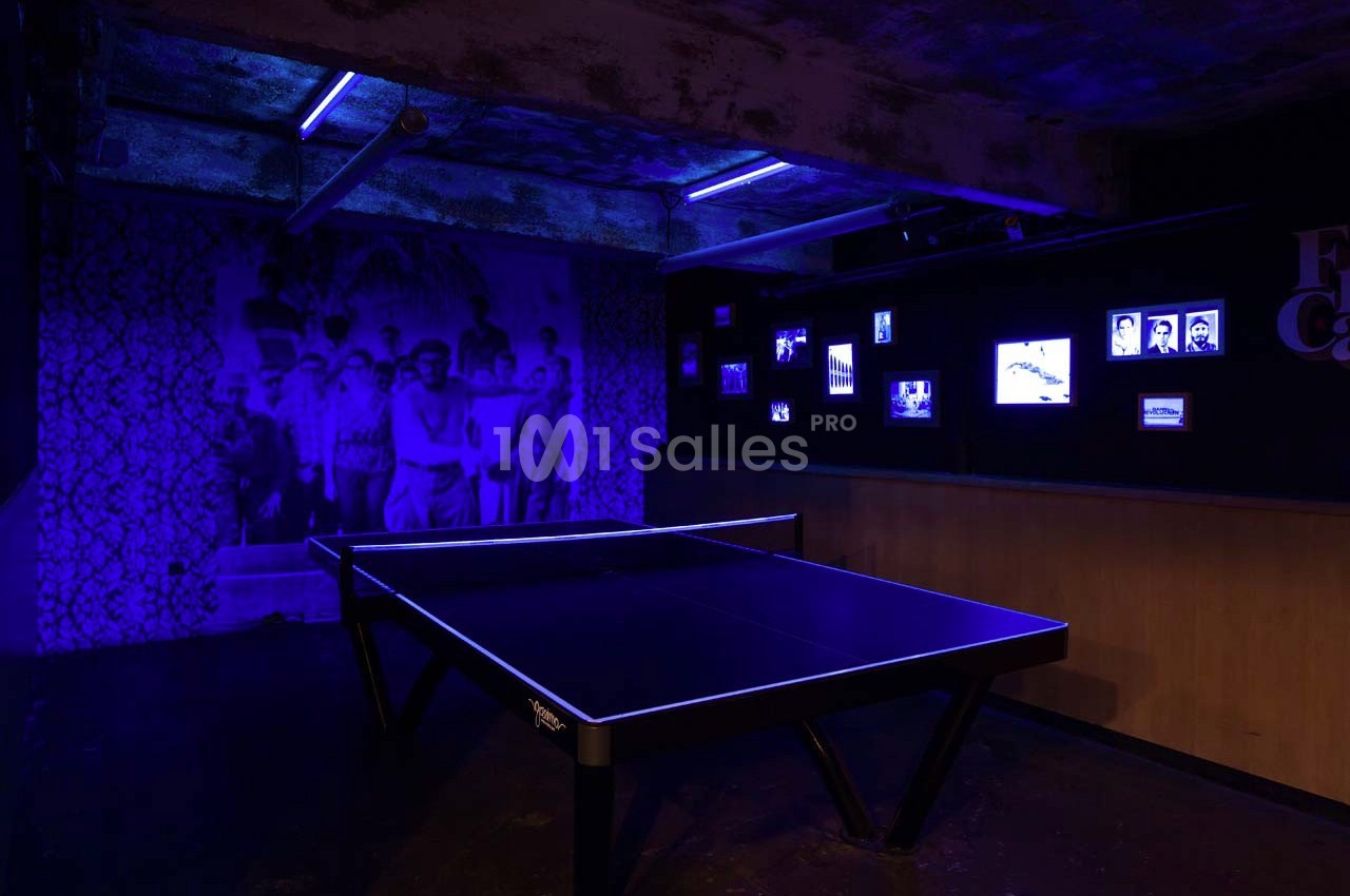 Table de ping-pong éclairée par des lumières violettes dans une pièce sombre avec des photos rétro sur les murs.
