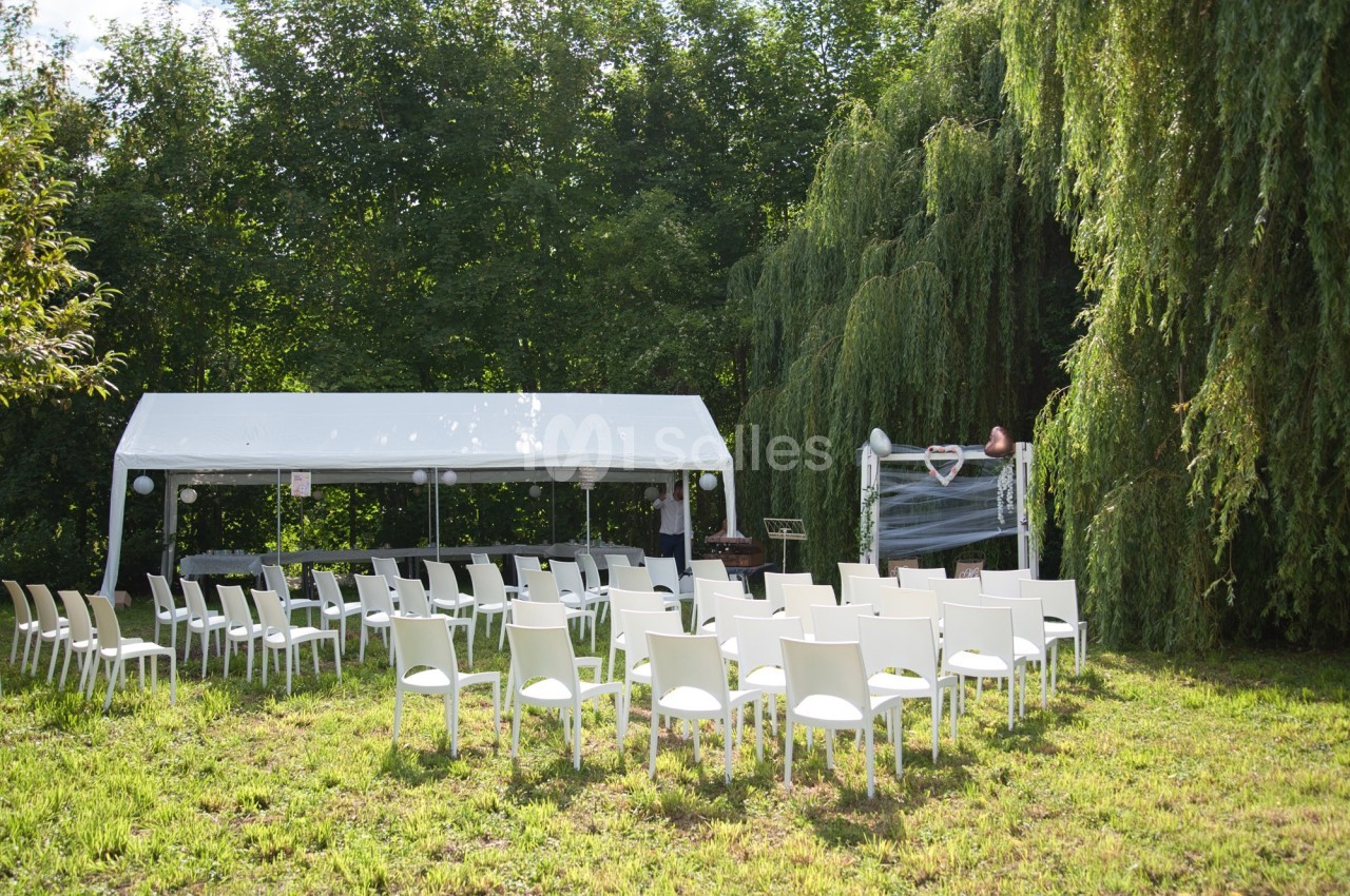 Chaises blanches disposées devant une tente blanche dans un jardin verdoyant, préparées pour un événement en plein air.