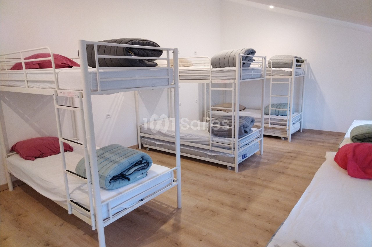 Dortoir avec plusieurs lits superposés équipés de matelas, draps et couvertures dans une pièce lumineuse au sol en bois.