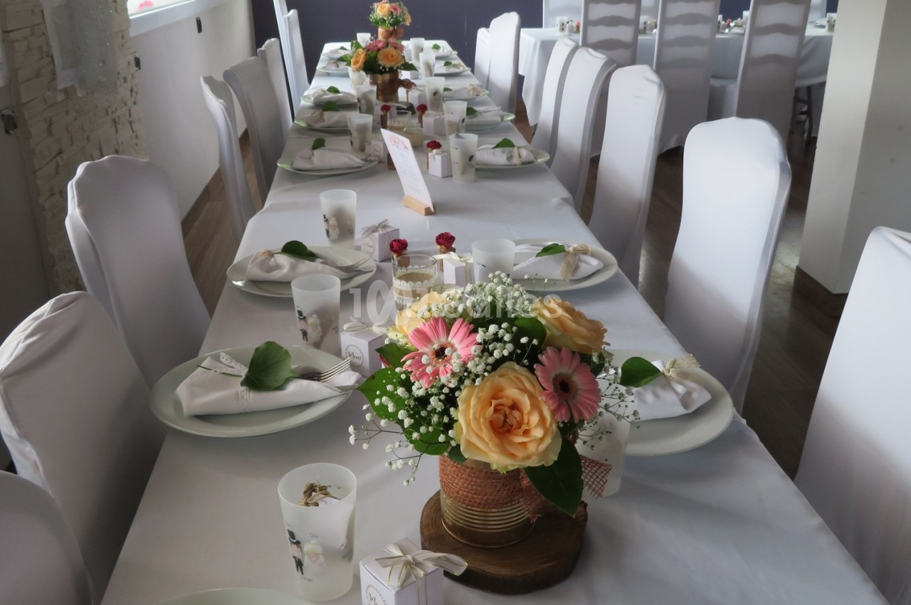 Table dressée pour un événement, décorée avec des fleurs colorées et des couverts disposés sur des nappes blanches.