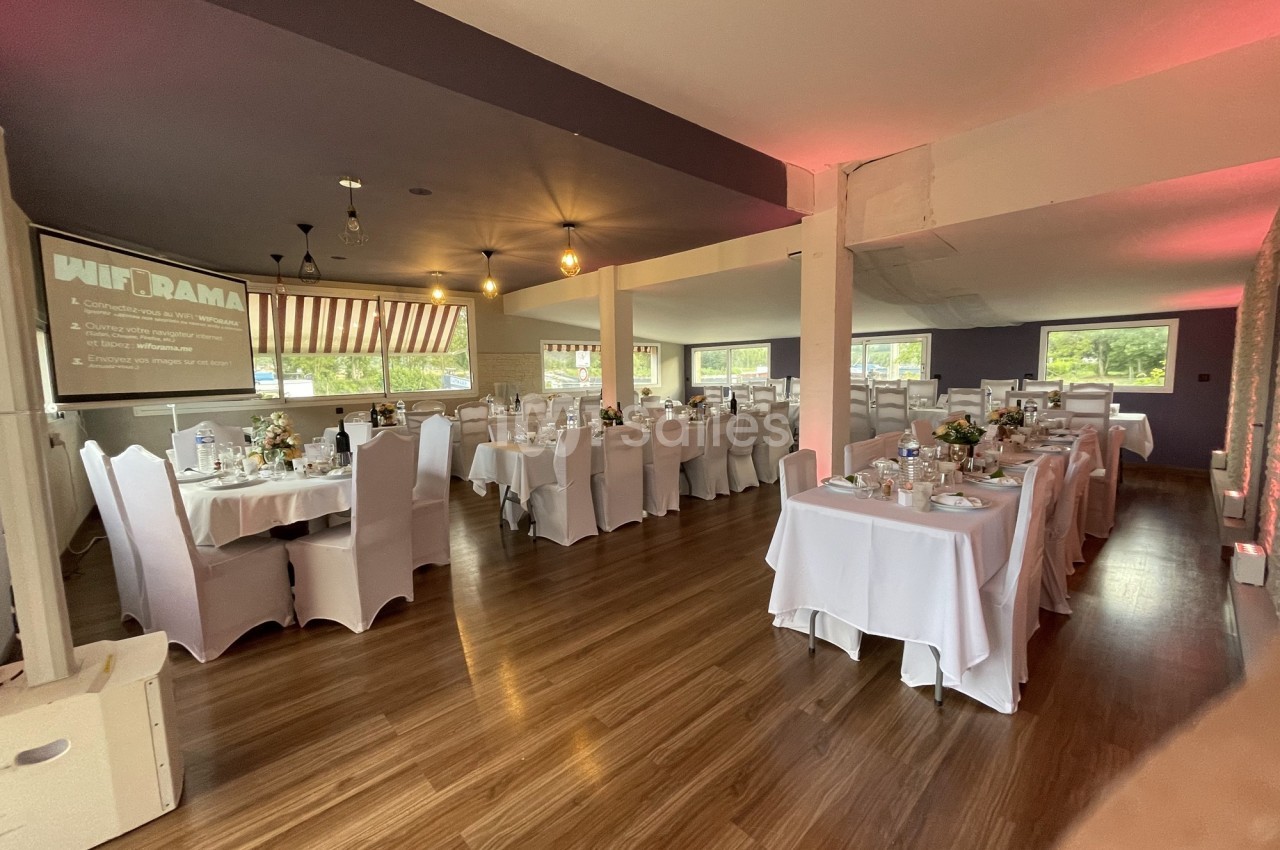 Salle de réception décorée avec des tables dressées pour un événement, éclairage chaleureux et vue sur l'extérieur.
