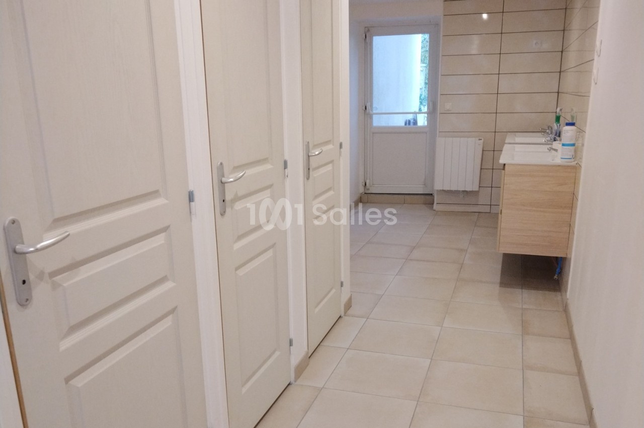 Couloir avec portes blanches menant à une salle d'eau équipée d'un lavabo et de carrelage beige au mur et au sol.