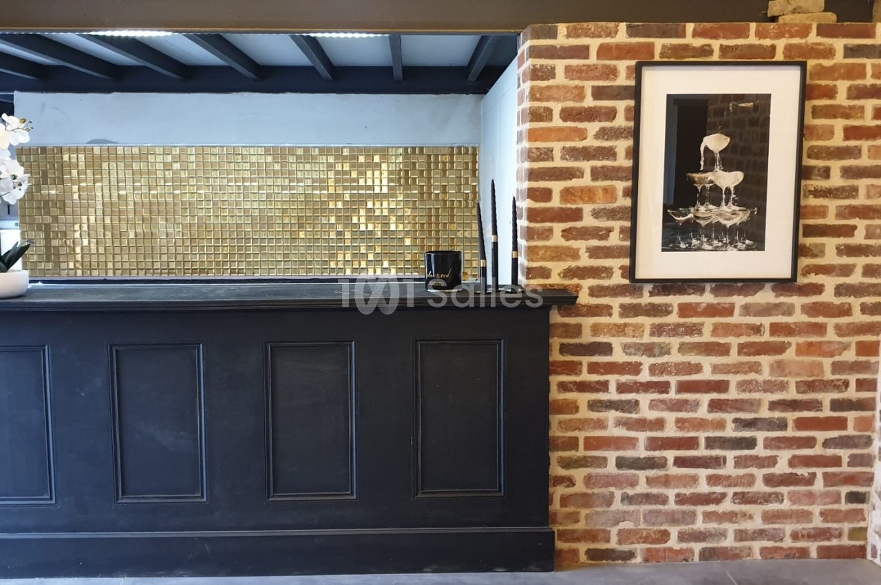Comptoir noir devant un mur en briques, décoré d'un cadre photo, d'une orchidée blanche et d'un fond doré.