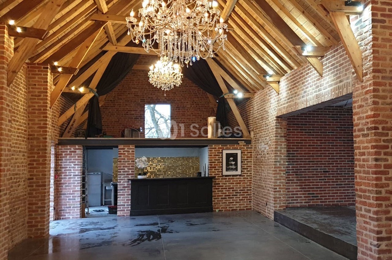 Intérieur d'une salle avec murs en briques, plafond en bois, lustres suspendus et une mezzanine au fond.