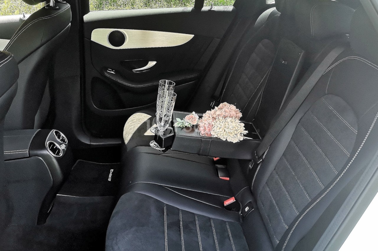 Intérieur d'une voiture avec des sièges en cuir noir, un bouquet de fleurs et deux flûtes à champagne posés à l'arrière.