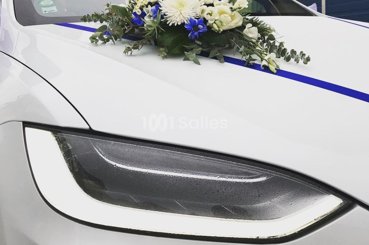 Gros plan sur le phare avant d'une voiture blanche décorée d'un bouquet de fleurs et d'un ruban bleu.
