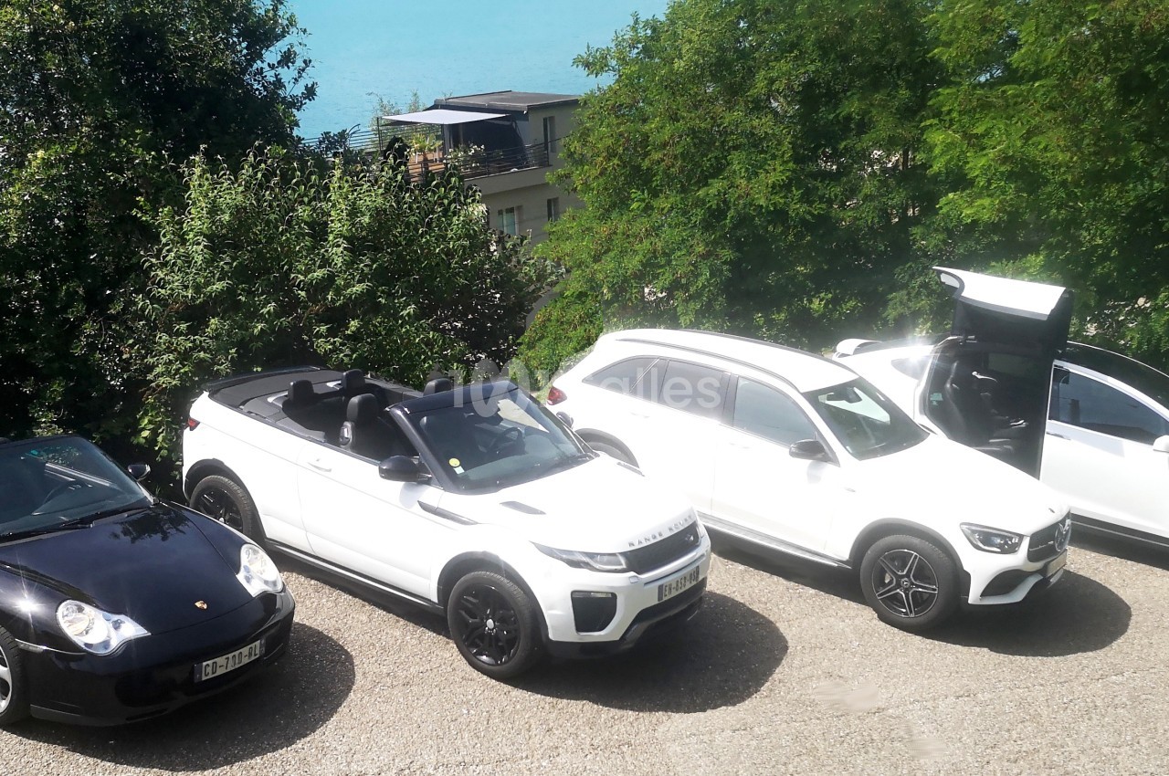 Quatre voitures, dont deux décapotables noires et blanches, stationnées sur un parking près d'un lac et d'arbres.