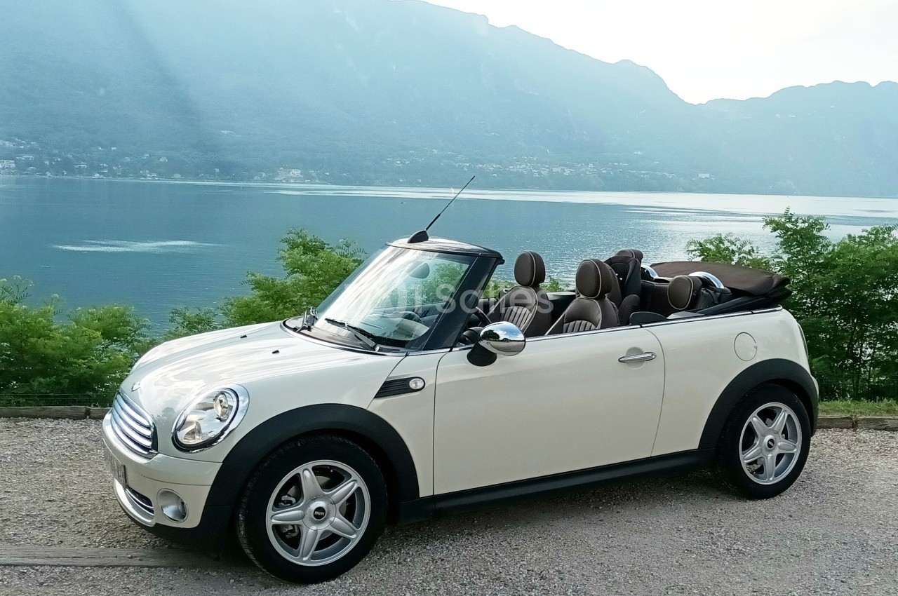 Voiture décapotable blanche stationnée devant un lac entouré de montagnes et de végétation.
