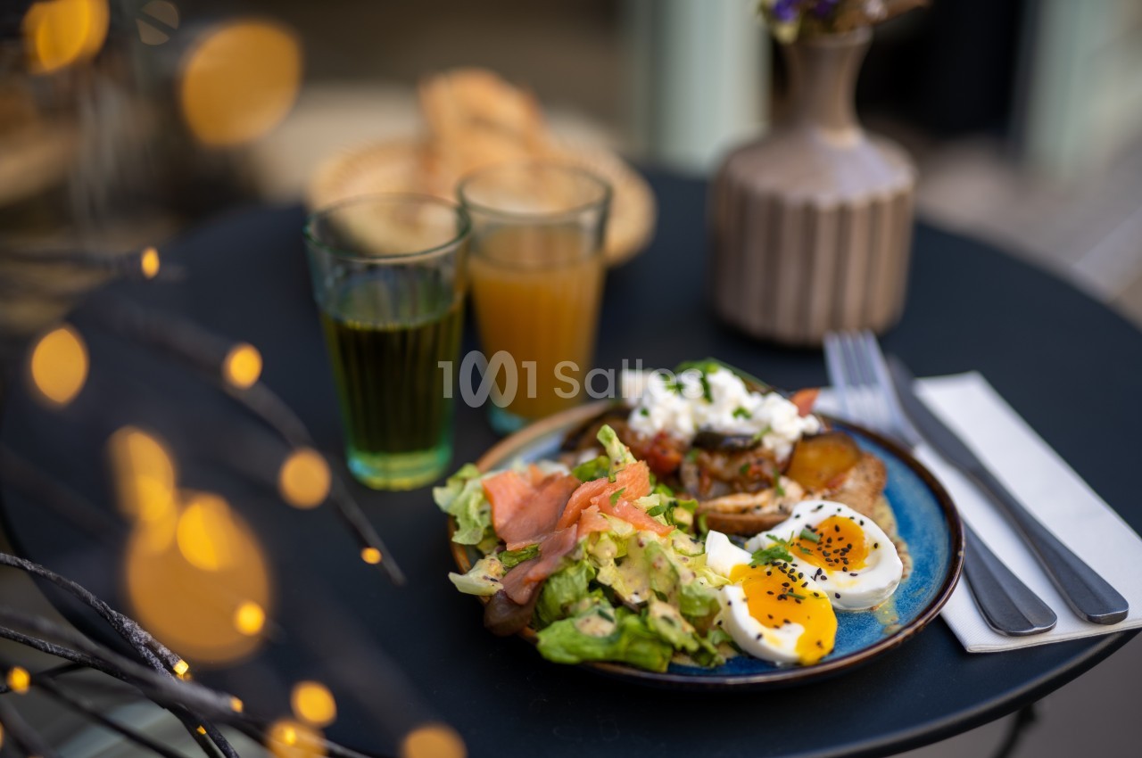 Assiette avec salade, saumon fumé, œufs mollets et légumes, posée sur une table avec deux verres de jus en arrière-plan.