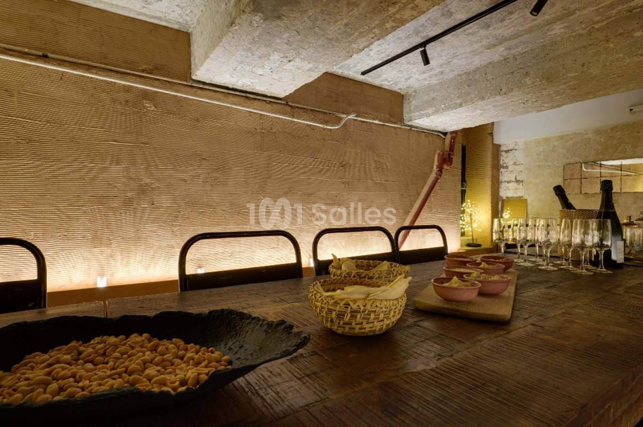 Table en bois avec des bols de snacks, des verres à pied et une bouteille, dans un espace à l'éclairage tamisé.