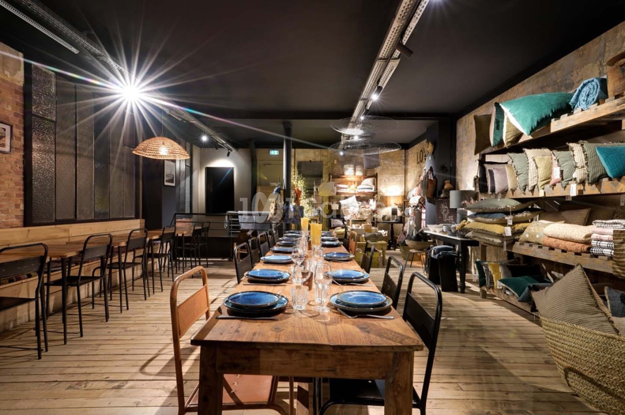 Salle de restaurant chaleureuse avec une longue table en bois dressée, éclairage tamisé et décoration rustique.