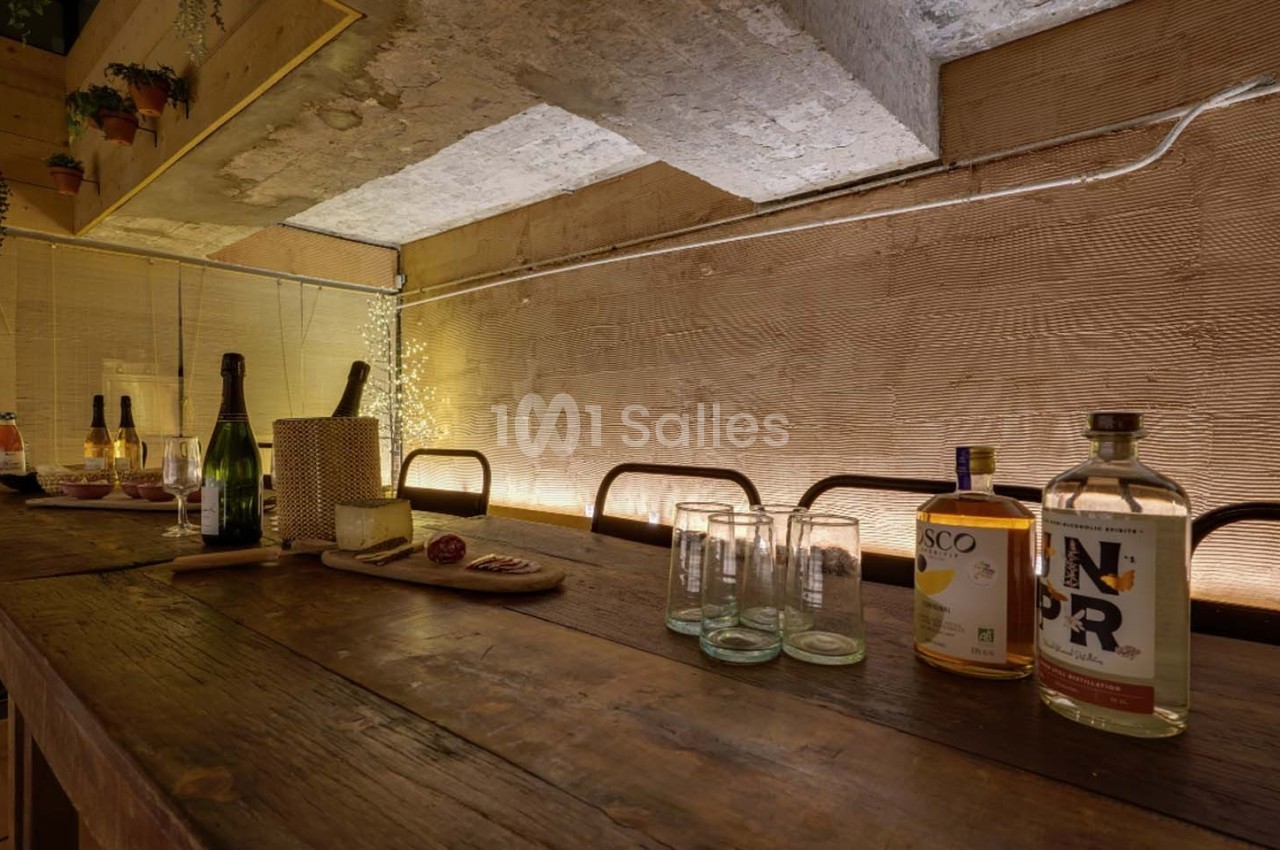 Table en bois avec bouteilles, verres et planche apéritive, dans un espace intérieur à l'éclairage tamisé.