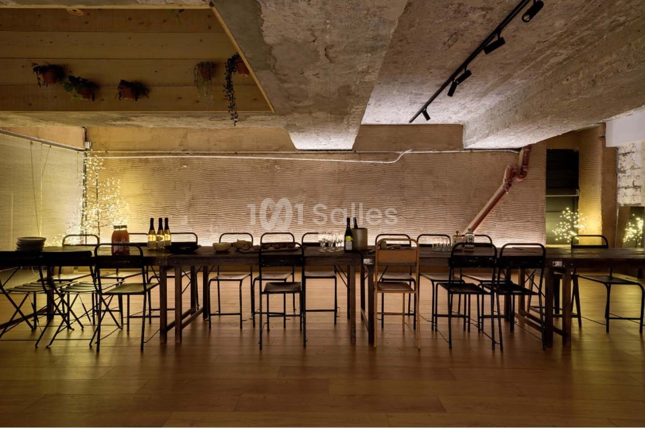Grande table en bois entourée de chaises dans une pièce au style industriel avec éclairage tamisé et murs texturés.