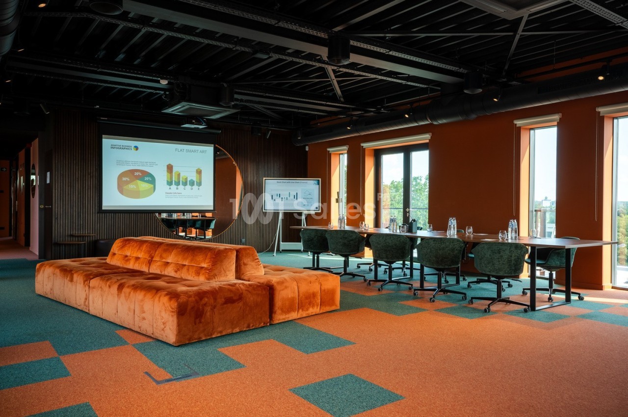 Salle de réunion moderne avec canapé orange, écran de présentation, tableau blanc et grandes fenêtres.