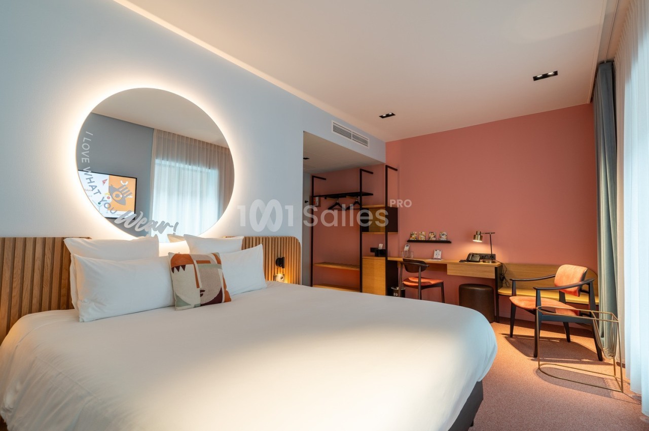 Chambre d'hôtel moderne avec lit double, bureau, chaise et éclairage doux, décorée dans des tons clairs et chaleureux.
